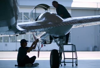 Aircraft in hangar with two aircraft maintenance technicians working on it